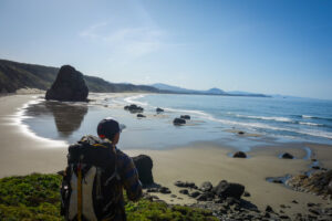 backpacker overlooking the expansive view of the oregon coast with haystacks and wide sandy beaches.