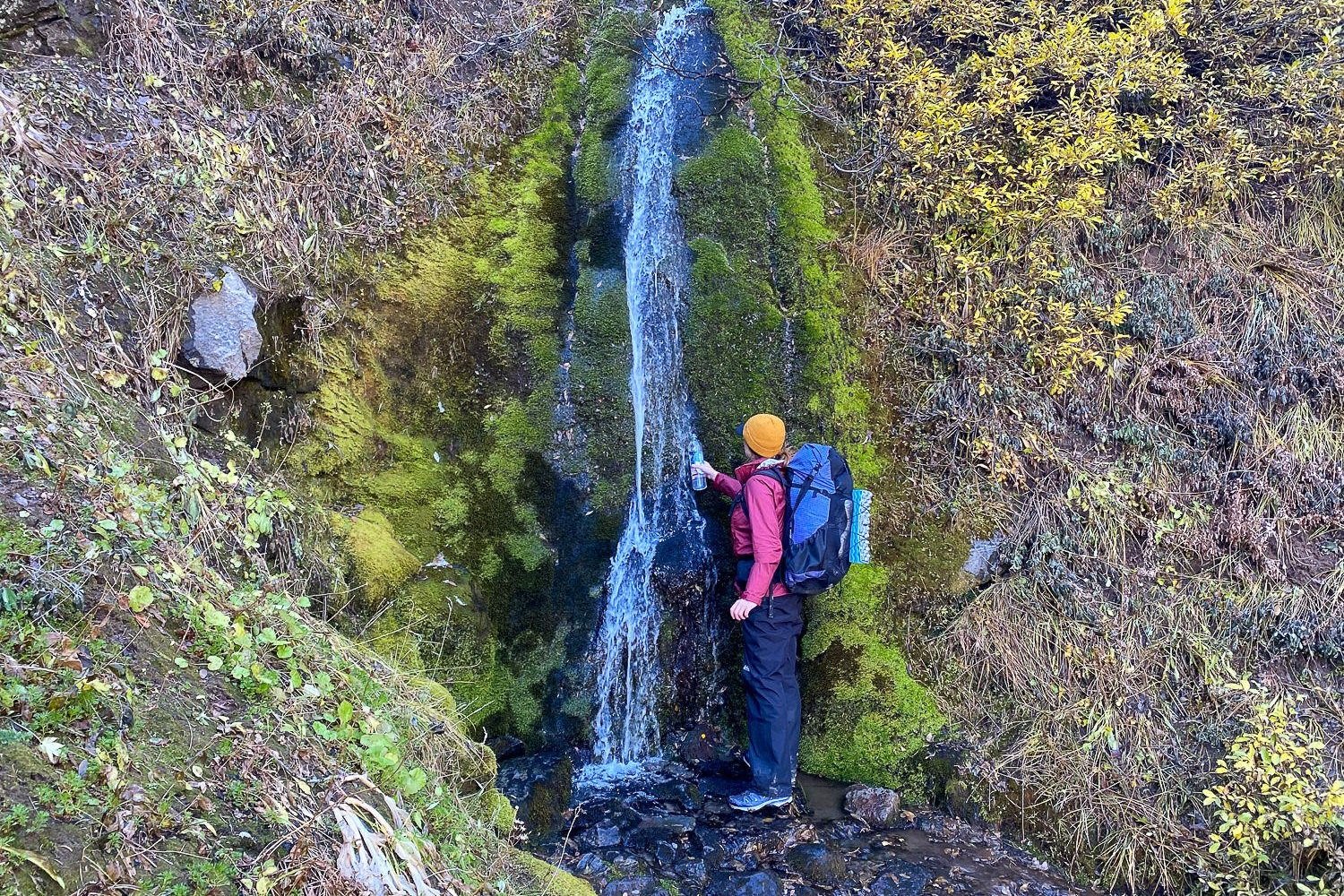 backpacker on the timberline trail filling up their water bottle from a small waterfall.