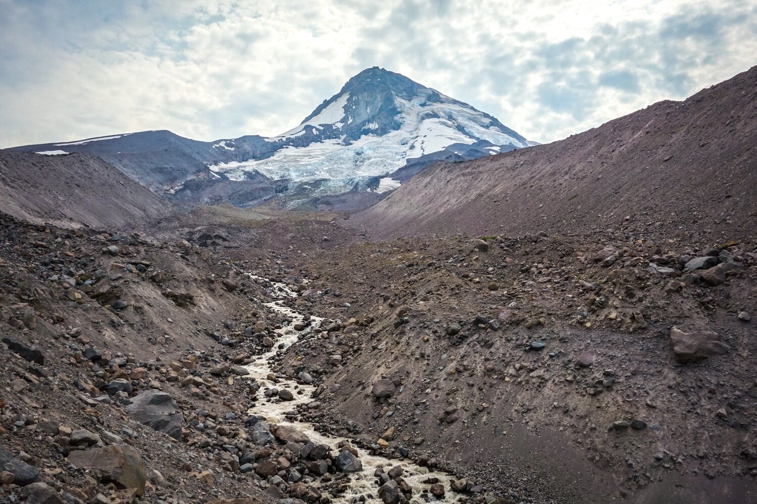 small creek filled with cloudy glacial runoff on below the snow capped peak of mt. hood. 