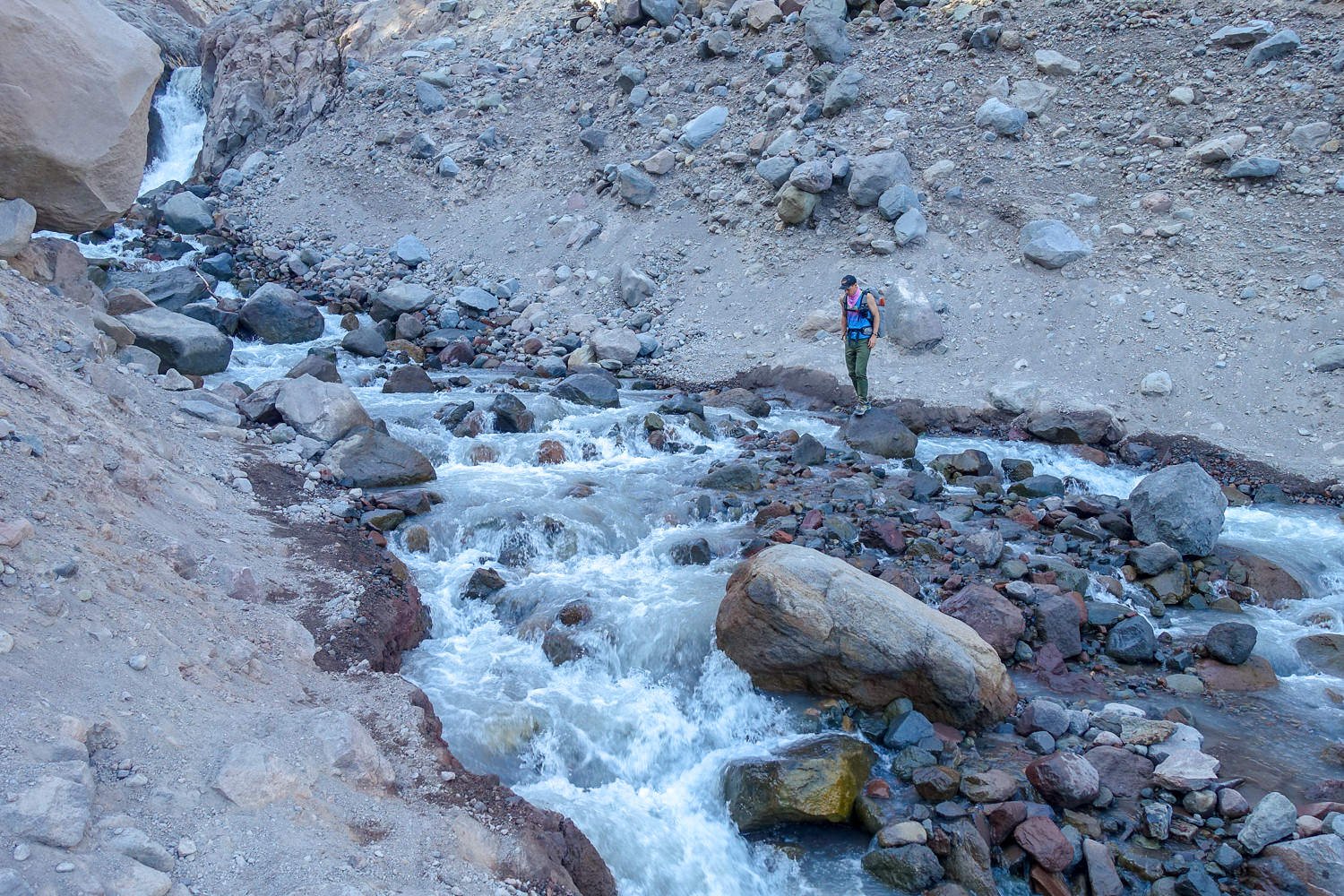 backpacker looks to cross a glacial creek on in a rocky ravine on mt. hood