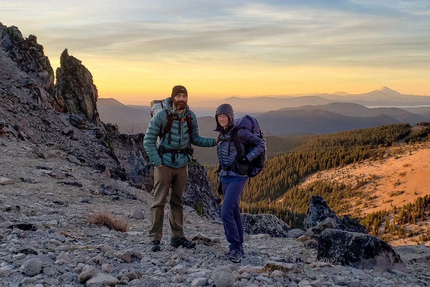 two backpackers bundled up on mt. hood watching the sunset over the cascade range