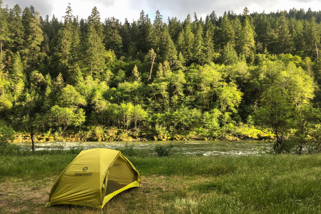 tent pitched on a grassy bar next to the rogue river