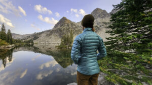 A backpacker standing by a mountain lake in a teal down jacket