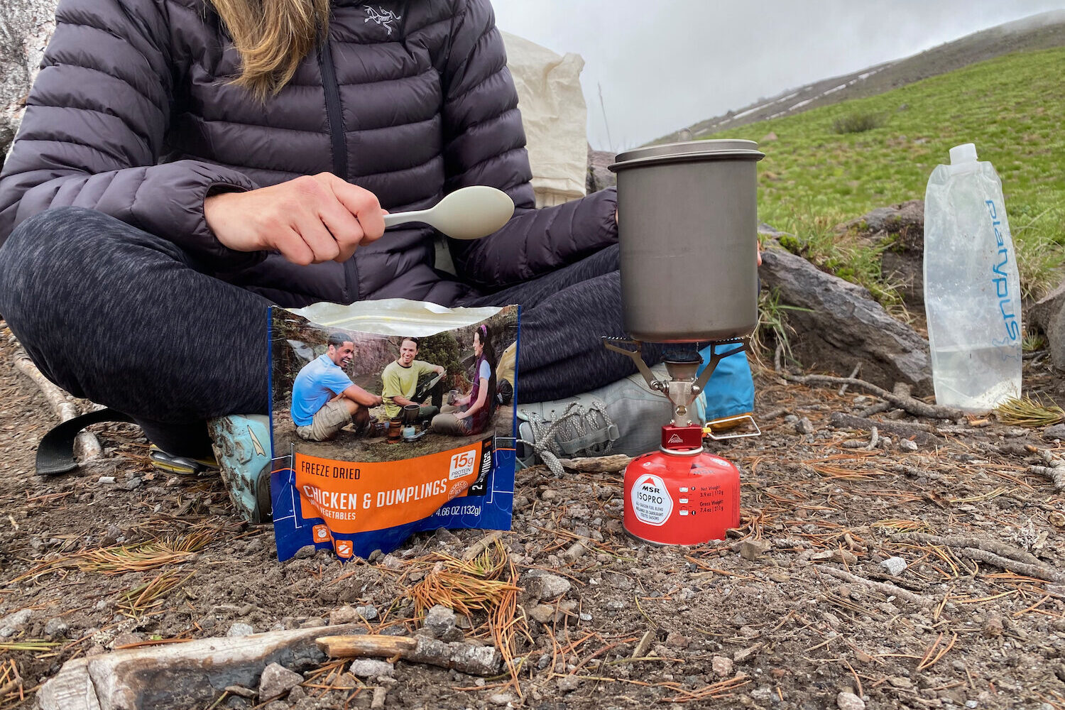 A backpacker next to a stove waiting for water to boil so she can pour it into a freeze-dried meal pouch.