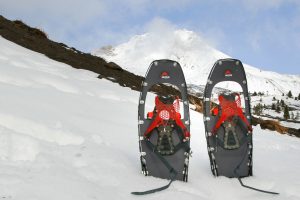 THE MSR LIGHTNING ASCENT SNOWSHOES with their heels stuck in the snow on a snowy slope with a mountain in the background