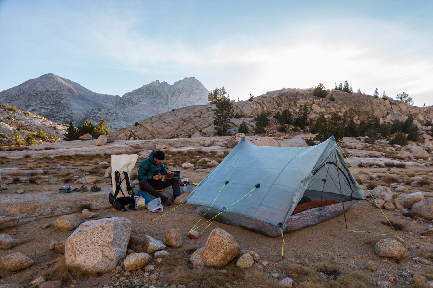 Backpacker on the the JMT eating dinner beside his tent and backpack