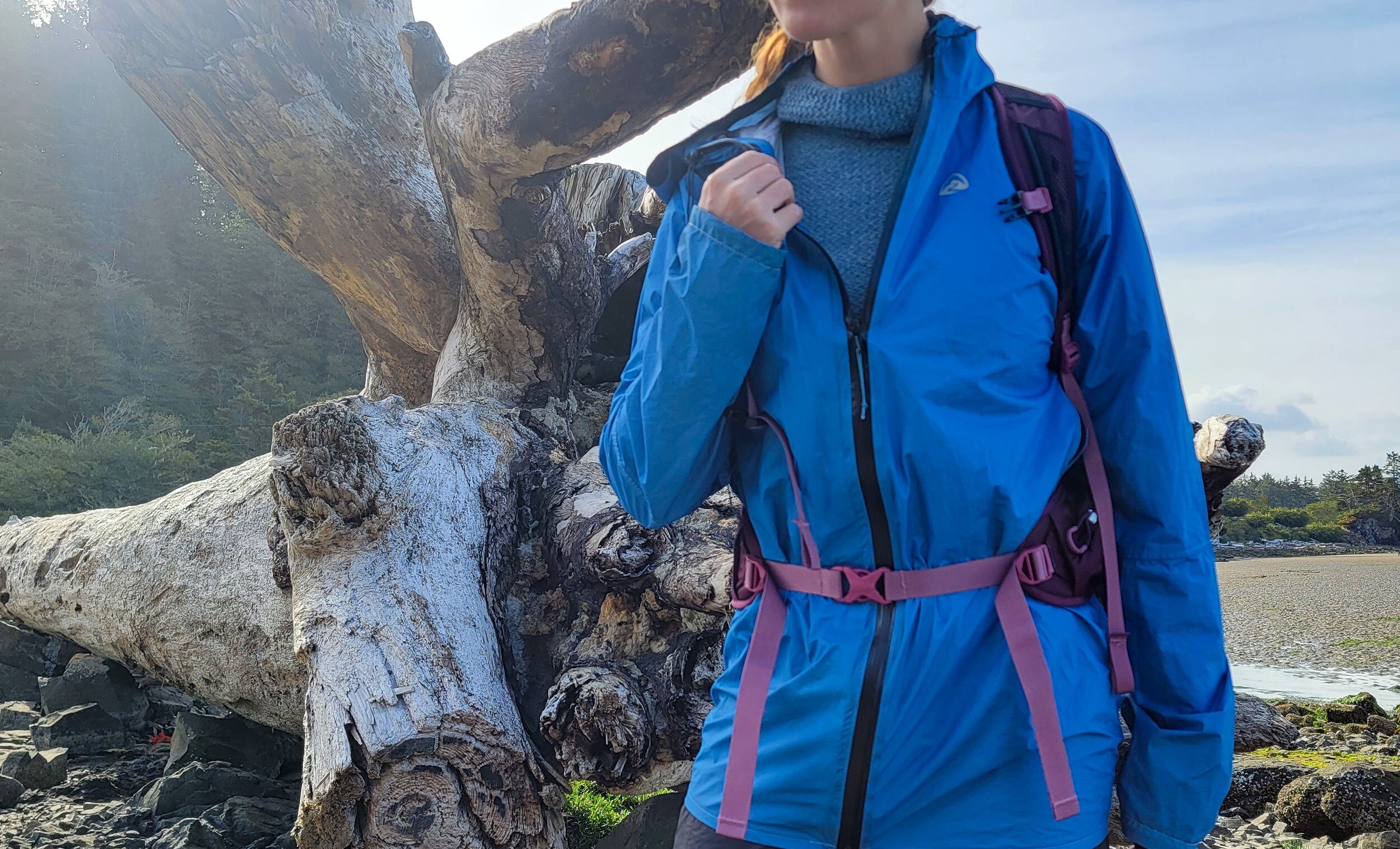 backpacker on the oregon coast by driftwood showing that they are wearing a warm baselayer under their jacket