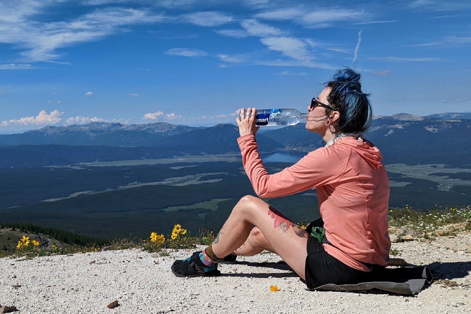 a hiker seated overlooking a valley and mountains on a sunny day drinking water treated by aquamira