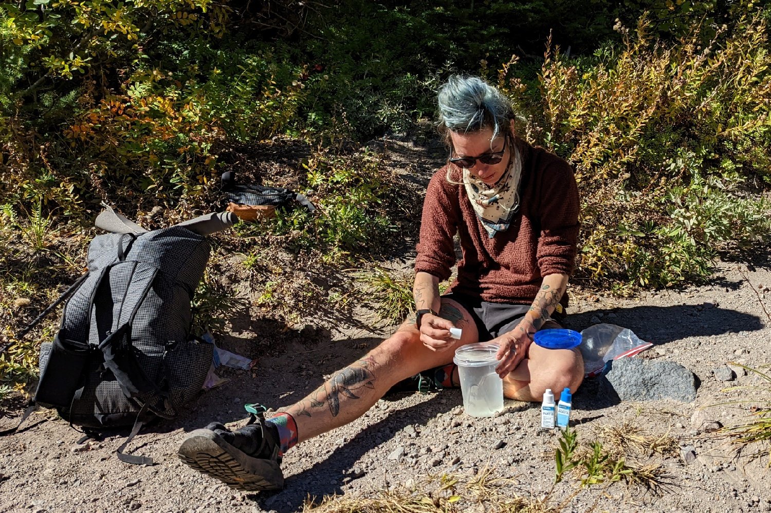 a backpacker taking a water break and treating their water with aquamira water purification droplets