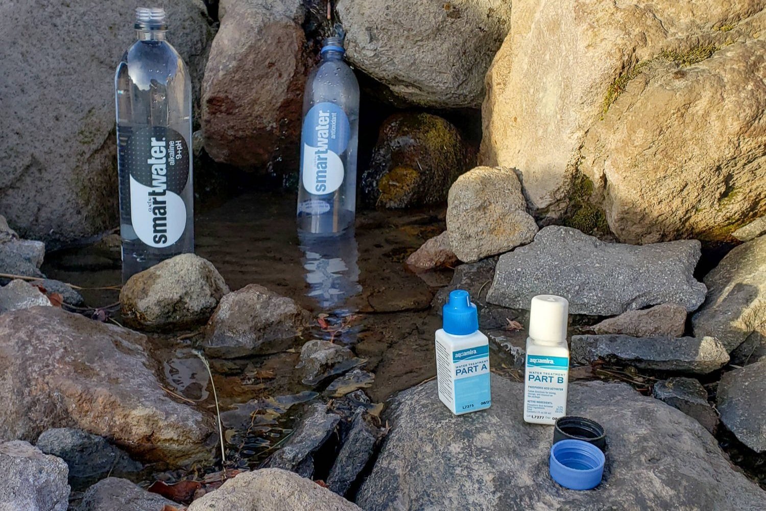 a person filling up smart water bottles from a small source seeping between the rocks