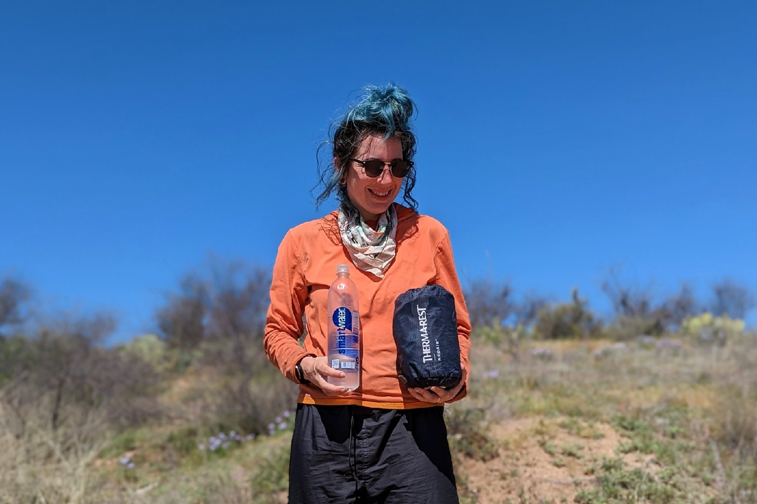 a hiker holds a one liter water bottle in one hand and the therm-a-rest NeoAir Xtherm NXT in the other to show how small it packs down to be.