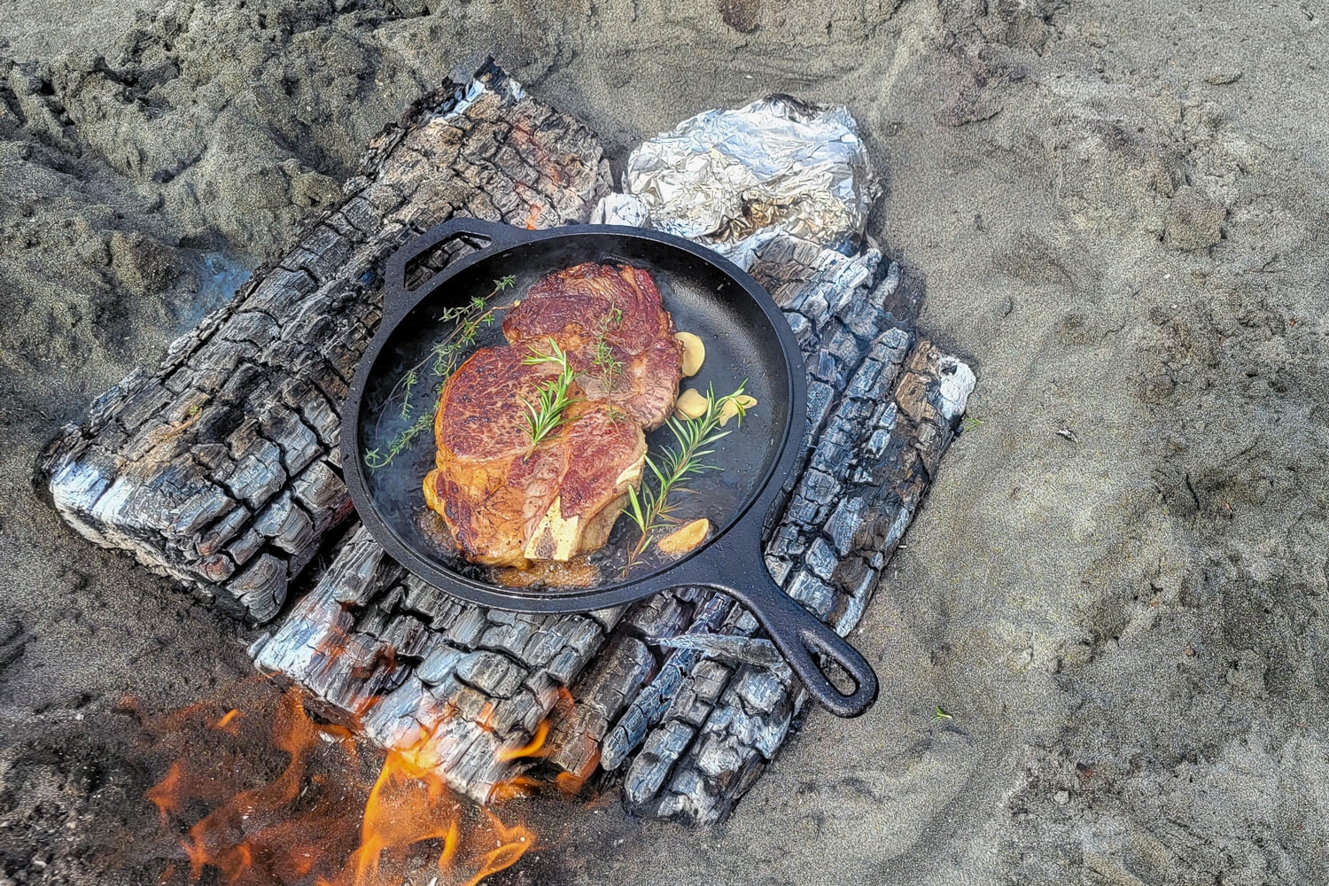 https://www.cleverhiker.com/wp-content/uploads/2023/08/Closeup-of-the-Lodge-Dutch-Oven-Combo-Cooker-cooking-a-steak-over-a-fire-on-the-beach.jpeg