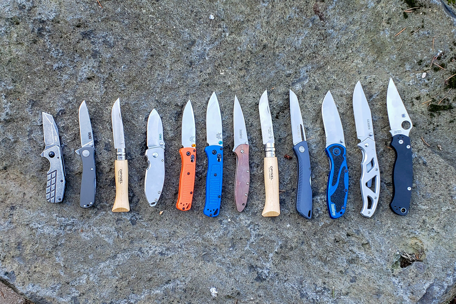 https://www.cleverhiker.com/wp-content/uploads/2023/08/The-best-pocket-knives-on-the-market-lined-up-on-a-rock.jpeg