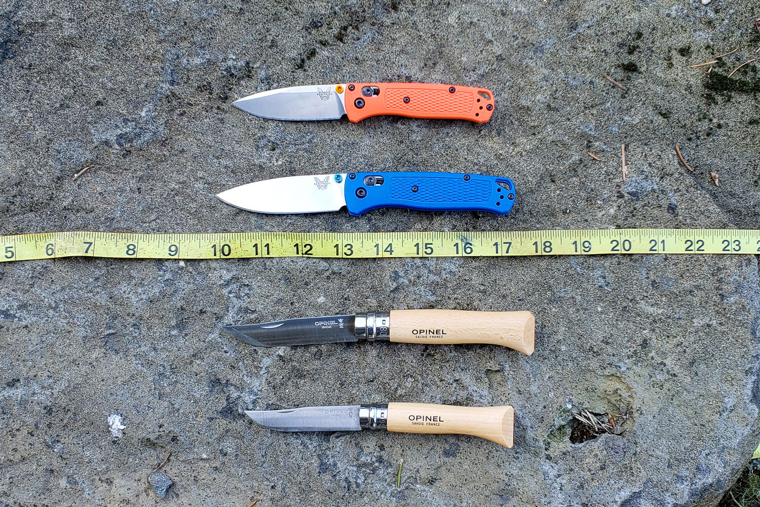https://www.cleverhiker.com/wp-content/uploads/2023/08/Top-down-view-of-full-size-pocket-knives-next-to-their-mini-counterparts-with-a-ruler.jpeg