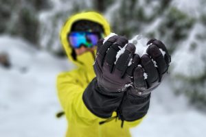 a person holding snow in their gloves with a ski jacket and goggle on