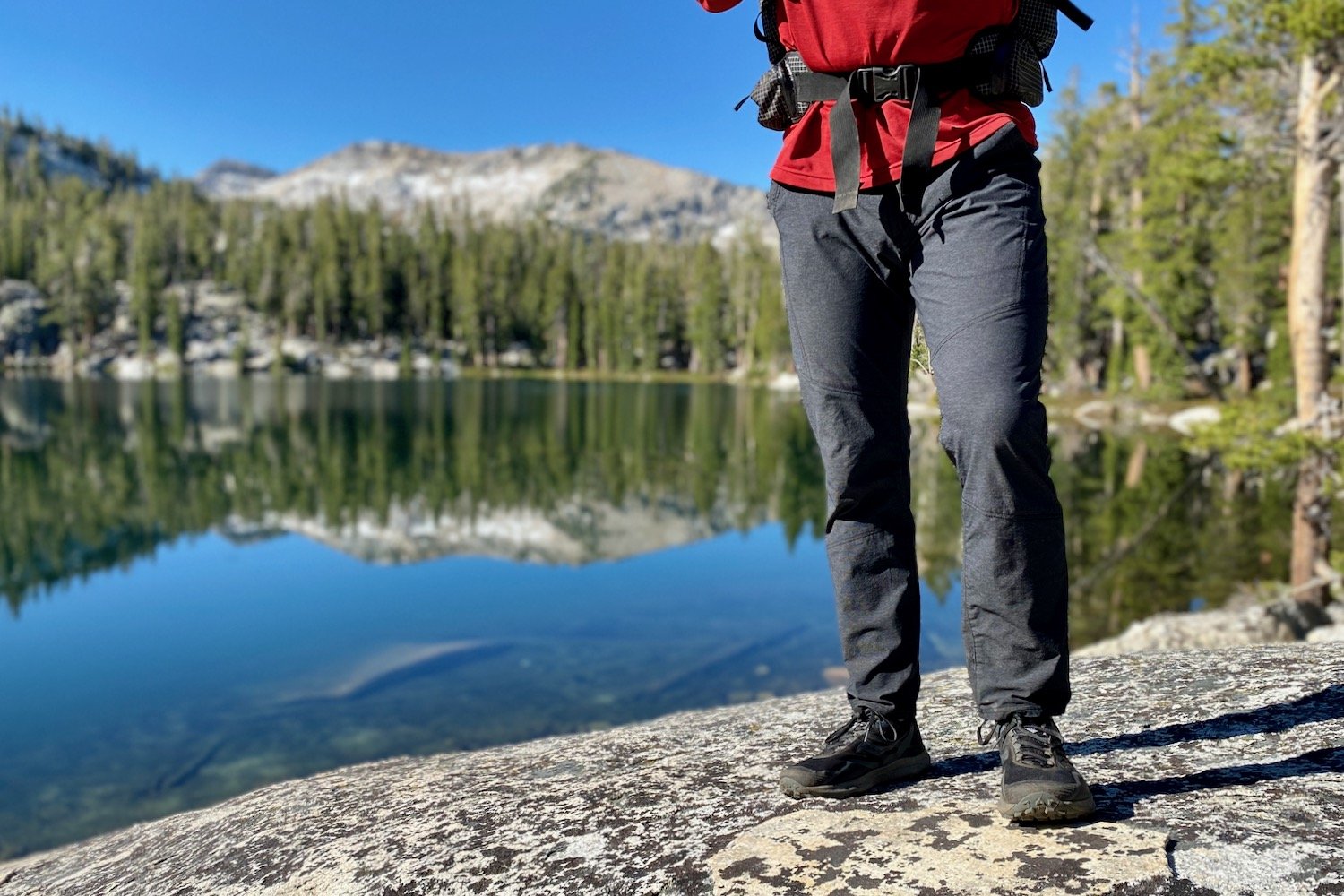 A backpacker standing in front of a lake in the men's Kuhl Deceptr hiking pants