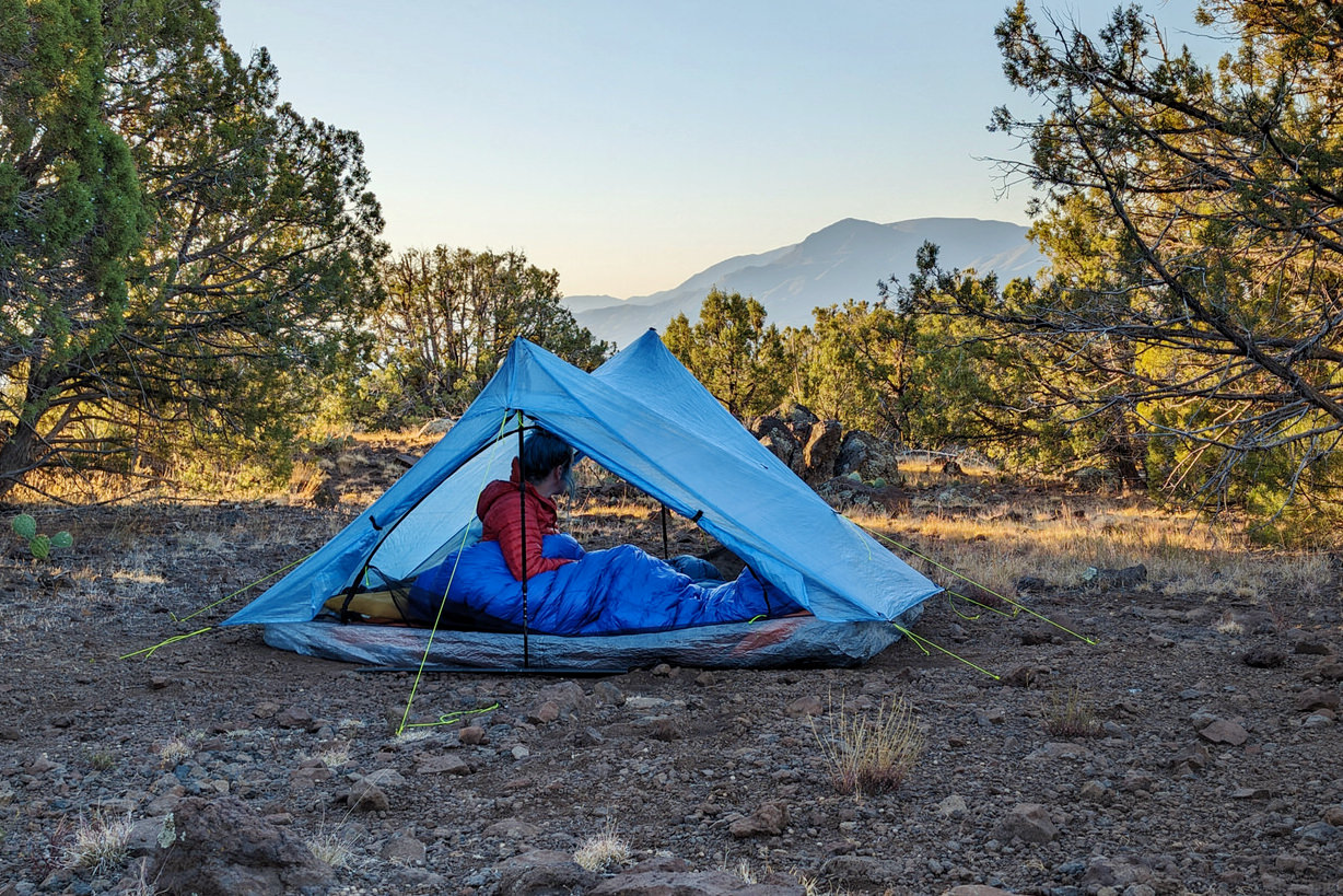 A hiker in the Zpacks Duplex Zip tent in the morning light with mountains in the background