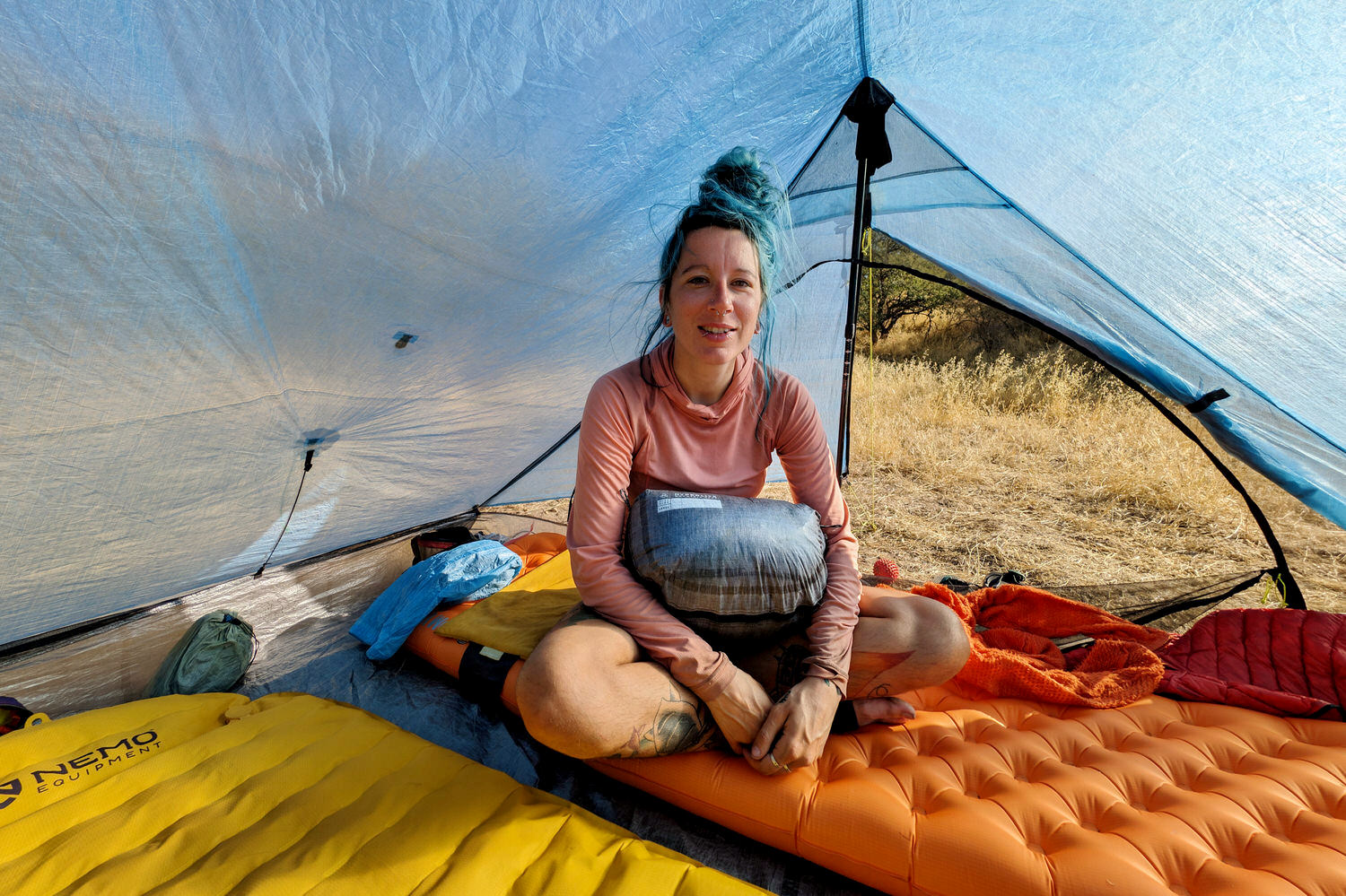 A hiker sitting inside the Zpacks Duplex Zip tent smiling at the camera with a stuff sack on her lap