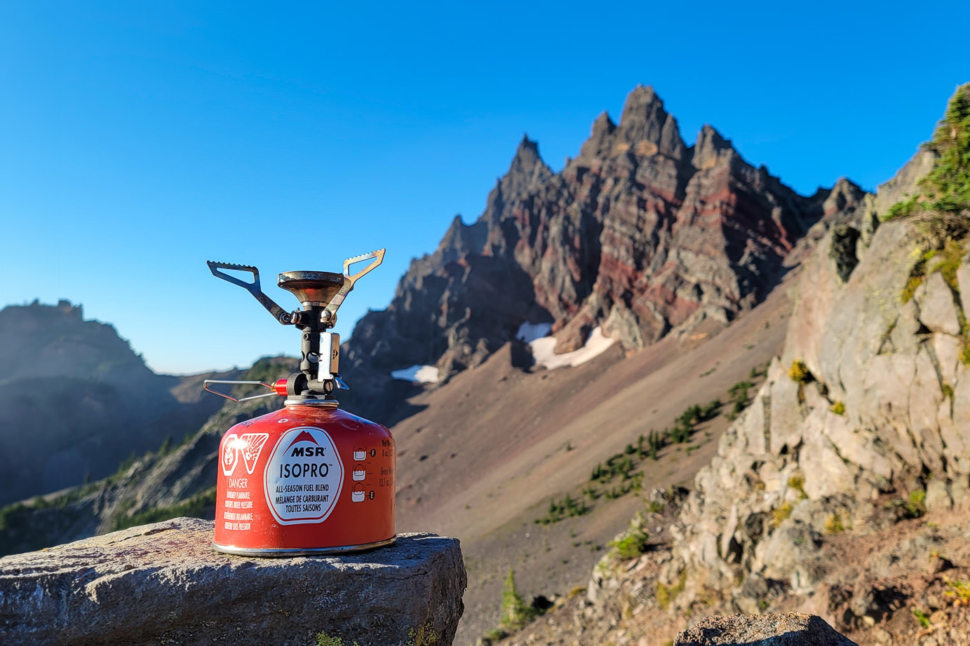 The MSR Pocket Rocket Deluxe backpacking stove in front of a jagged mountain with red bands