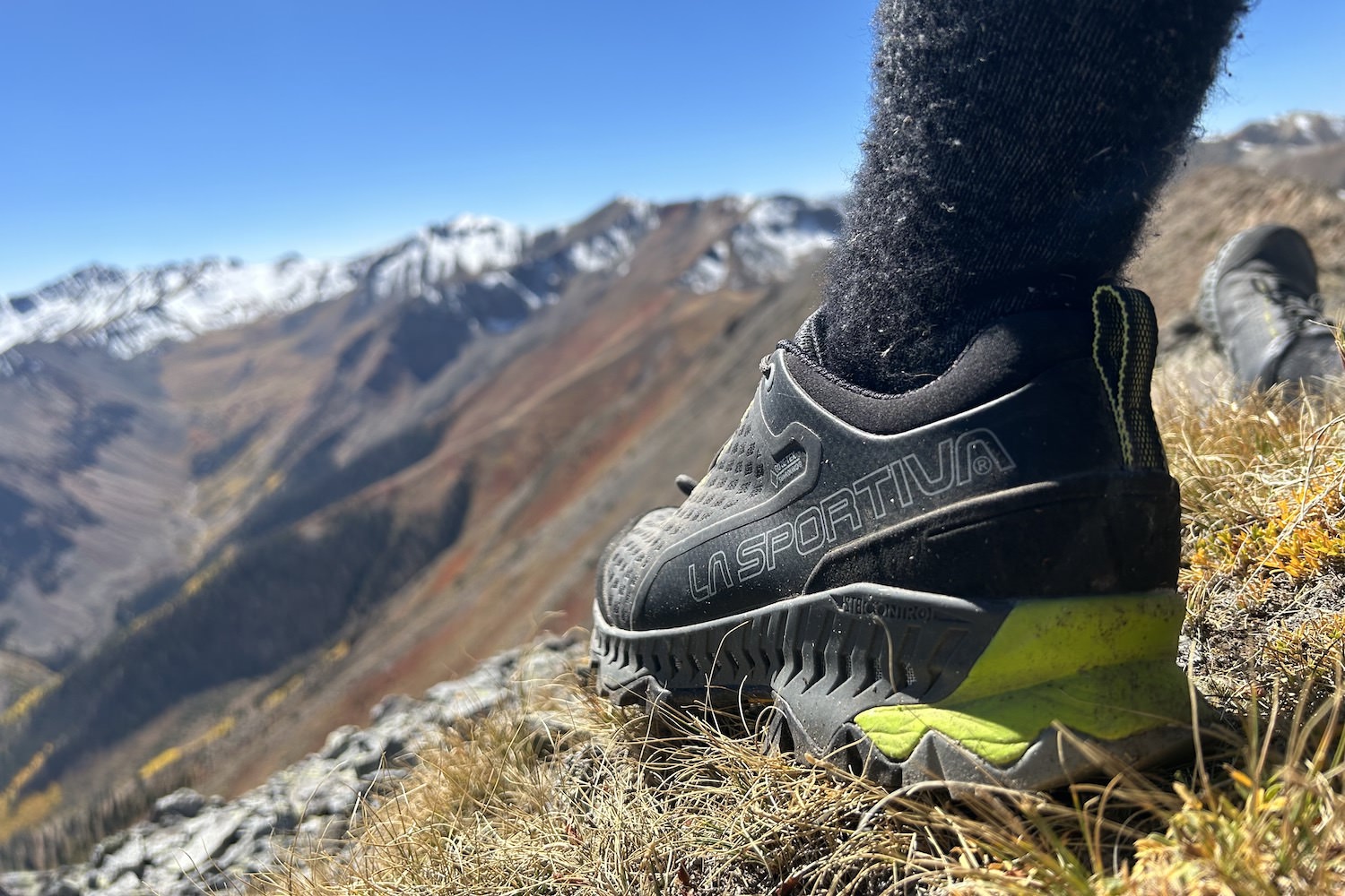 The La Sportiva Spire GTX men's hiking shoes in the foreground with a blurry view of snow-capped Colorado mountains in the distance