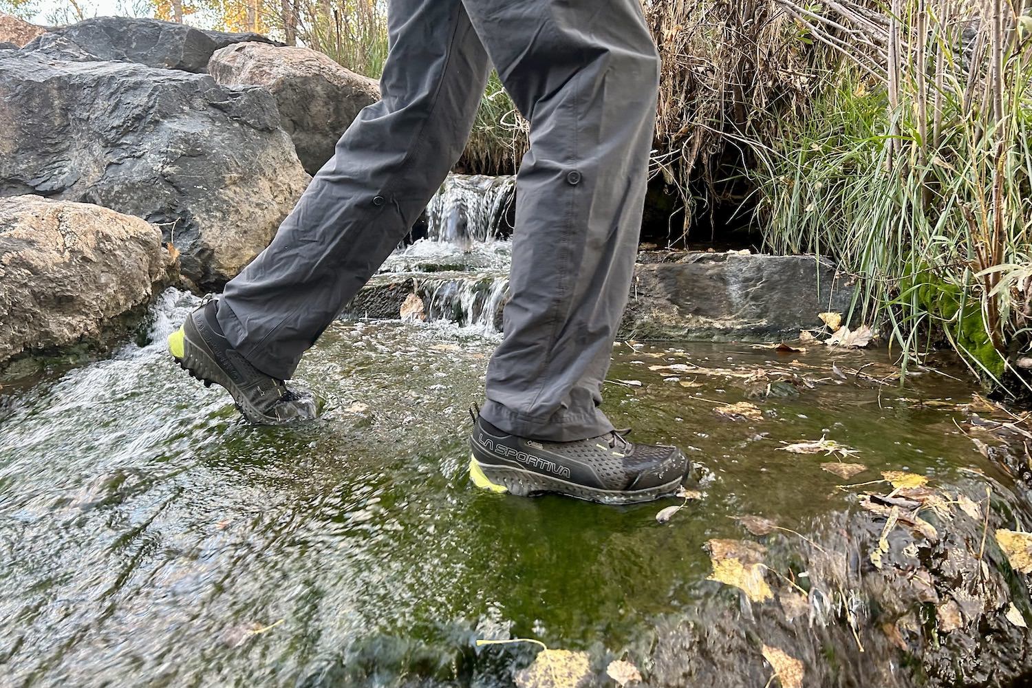 The lower half of a hiker crossing a flowing creek in the La Sportiva Spire GTX shoes
