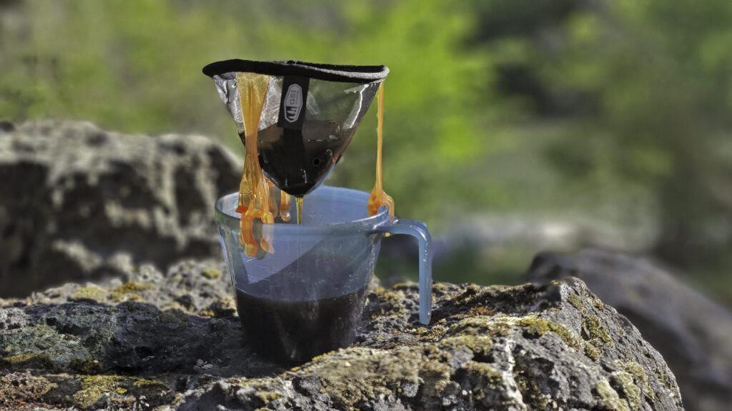 Closeup of the GSI Outdoors Ultralight Java Drip brewing coffee into an ultralight backpacking cup on a volcanic rock