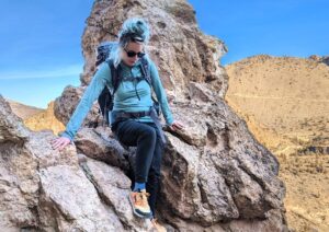 A hiker climbing down some rocks in a desert landscape wearing the REI Midweight Half Zip Base Layer