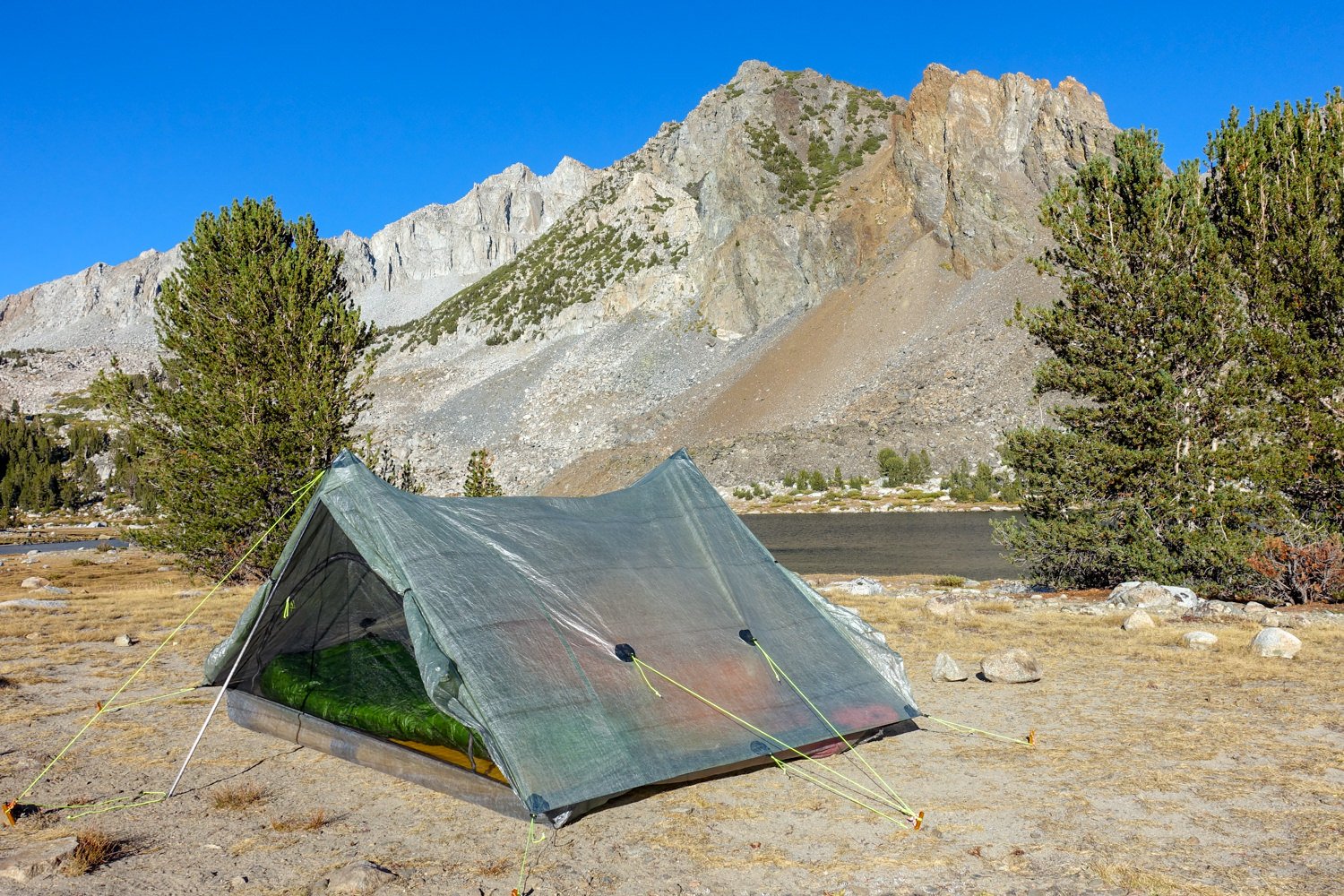 the zpack triplex ultralight tent set up below a rocky peak in full sun