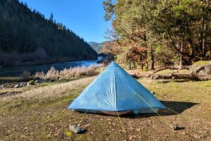 the zpacks plex solo tent pitched near a river on a sunny day