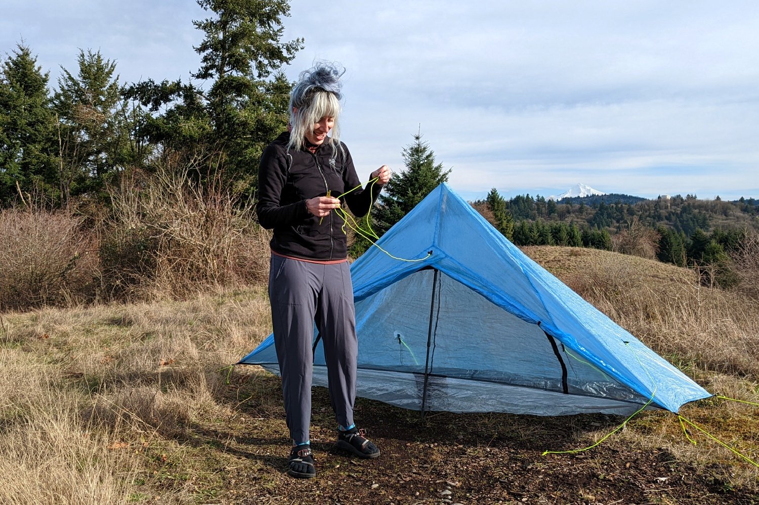 a backpacker setting up the guylines of the zpacks plex solo tent in a meadow