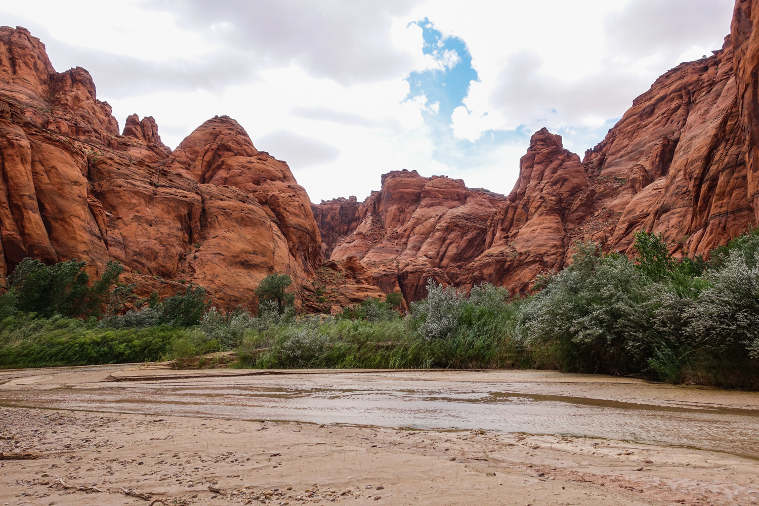 a redstone rock formation with a brown river and wide washout next to it in utah