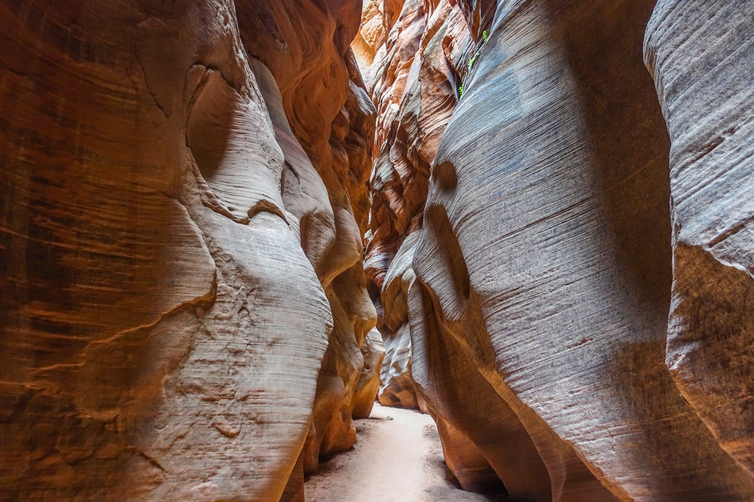 the sandy and narrow path through a slot canyon with red and orange sandstone cliffs on both sides