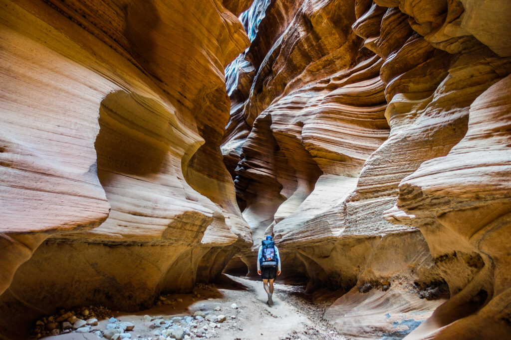 a backpacker walks below waves of sandstone cliffs