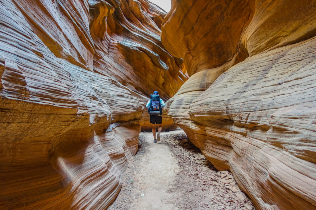 a backpacker enjoys the solitude of the narrow canyon where he can't see far ahead because of the undulating canyon walls