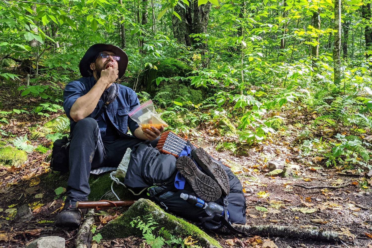 Appalachian Trail thru-hiker stopped on the trail eating snacks in the forest.