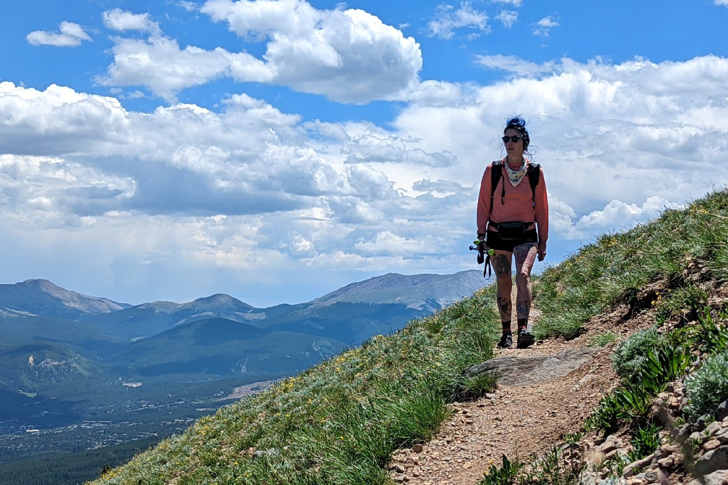 backpacker walking on the side of a mountain with mountains in the background on the colorado trail on a sunny day.