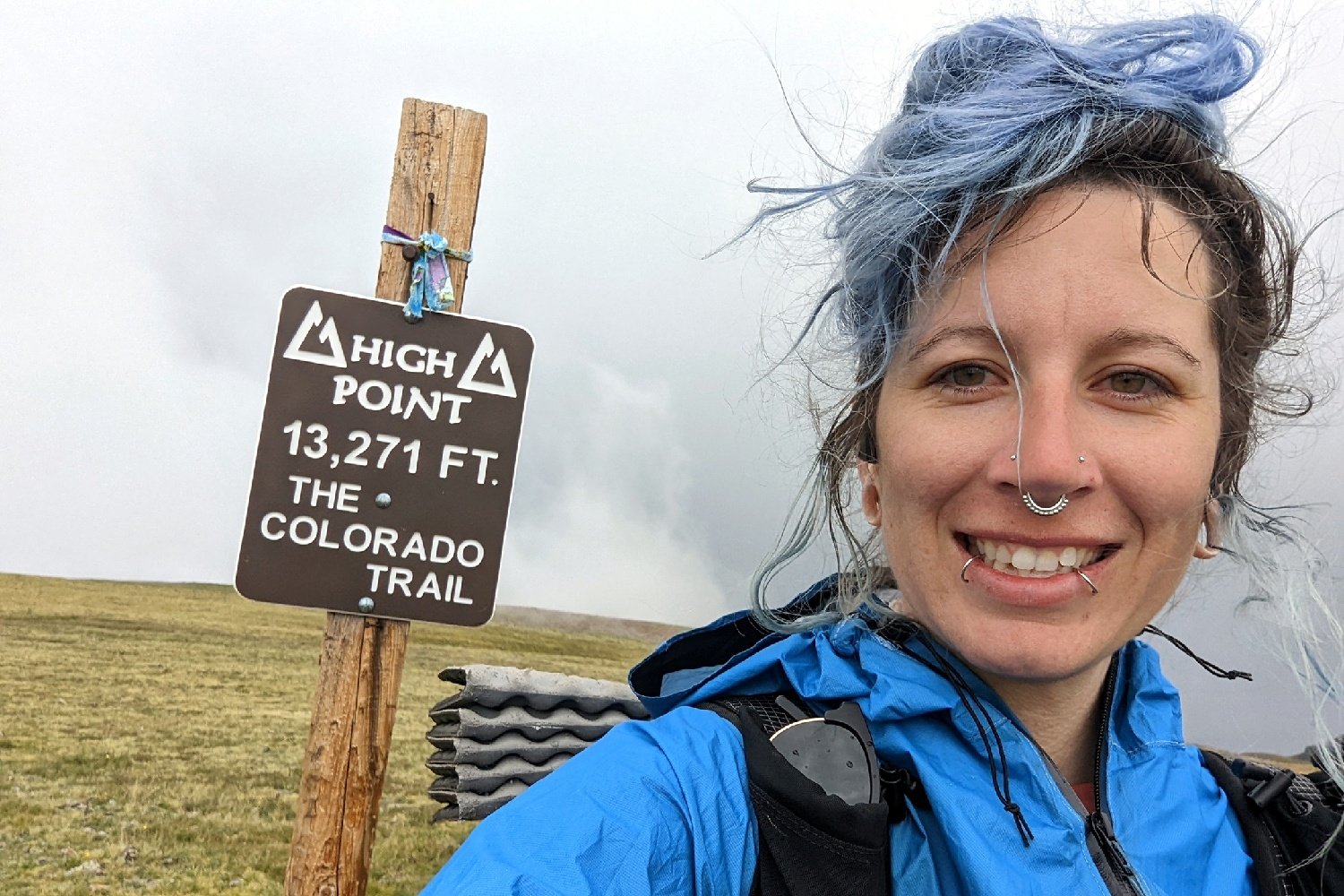 colorado trail thru-hiker posing in front of a trail sign that says "high point 13,271 ft the colorado trail"