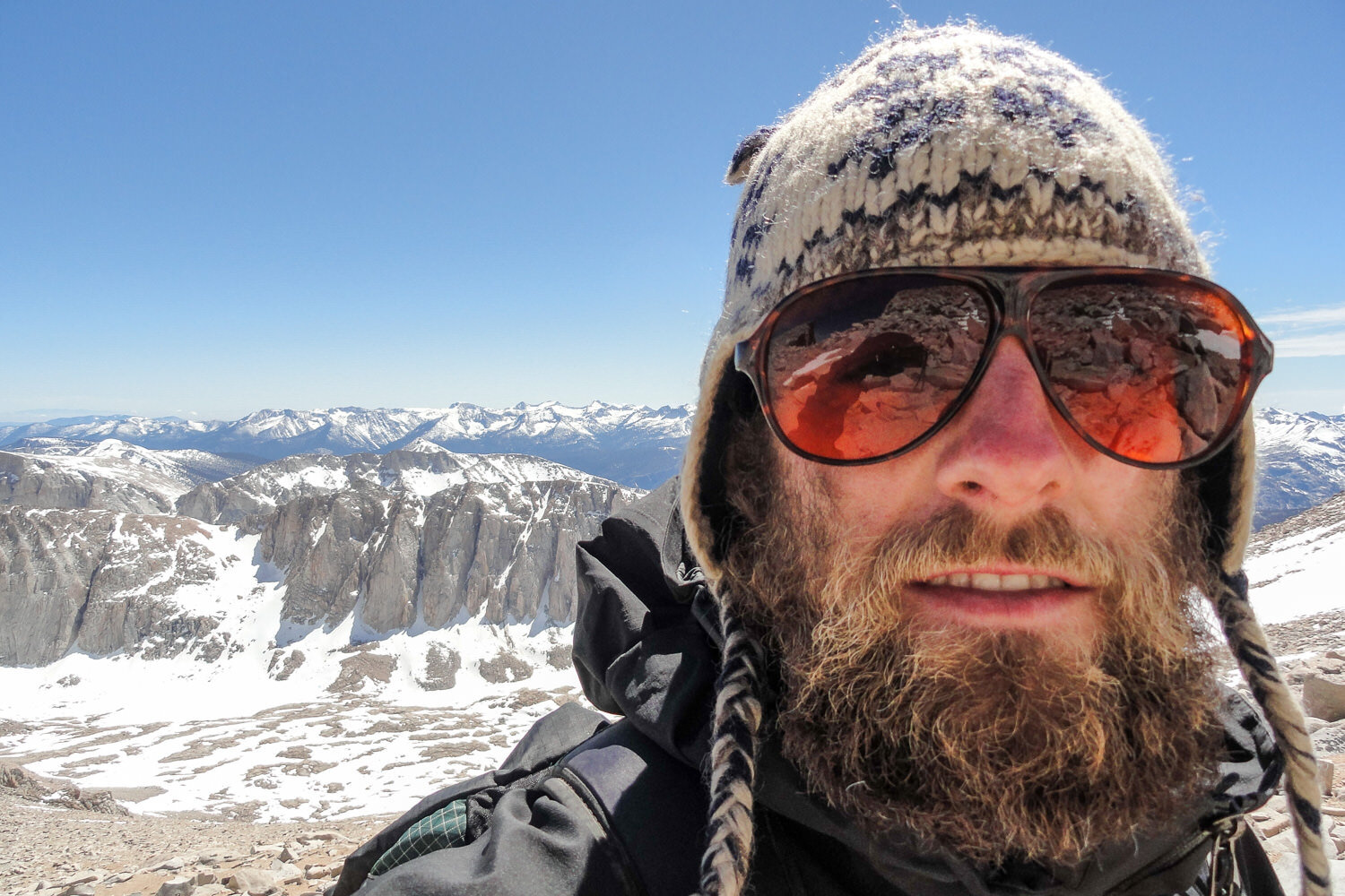 Thru-hiker with hat and sunglasses on with snowy mountains and blue sky