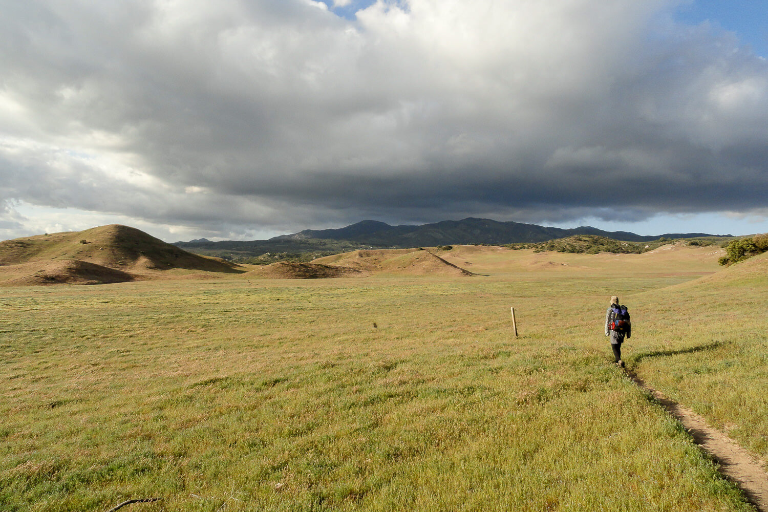 Hiker walking open plains headed toward rolling mountains