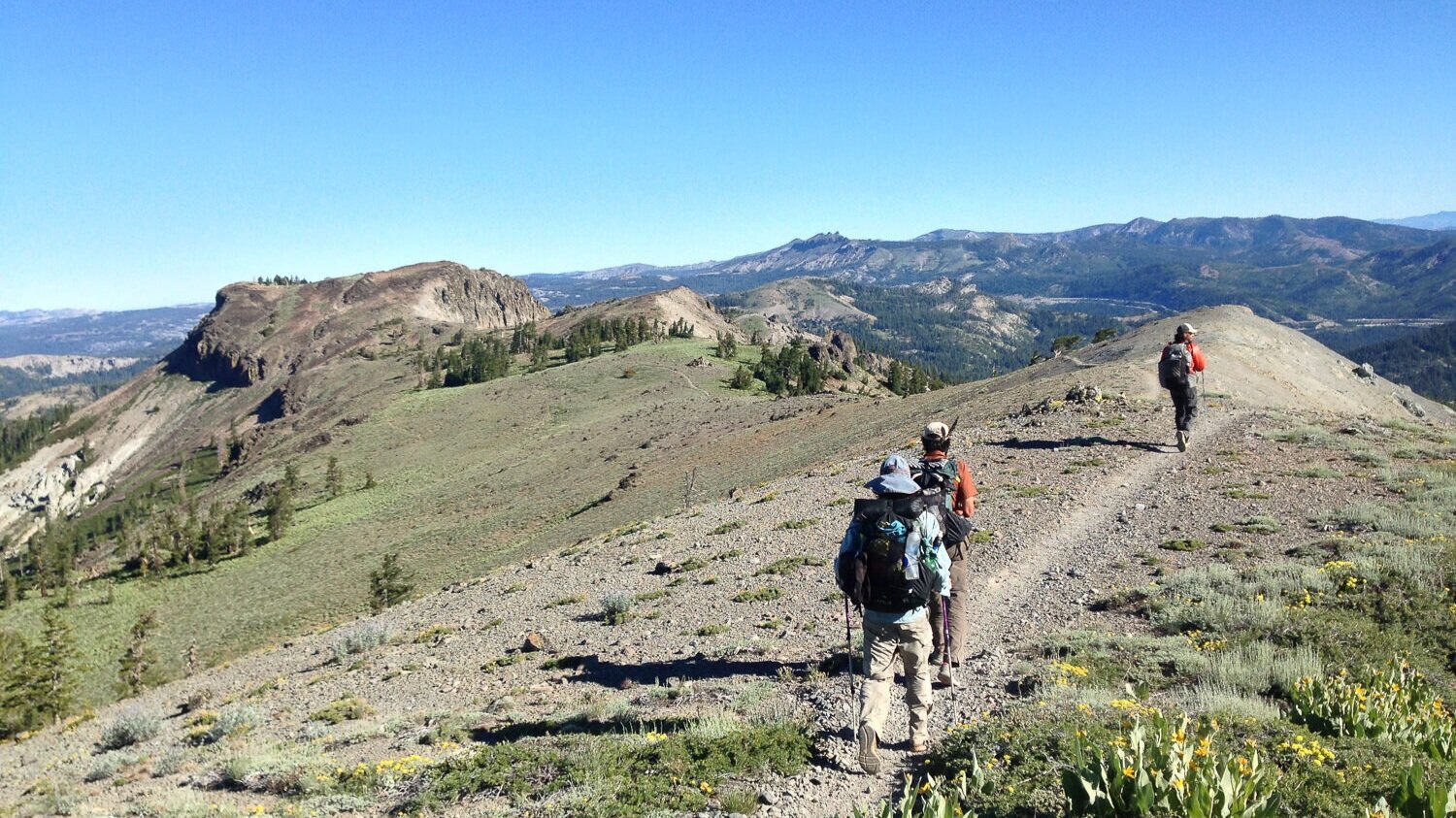 Three backpackers walking across a ridge line on a beautiful sunny day.