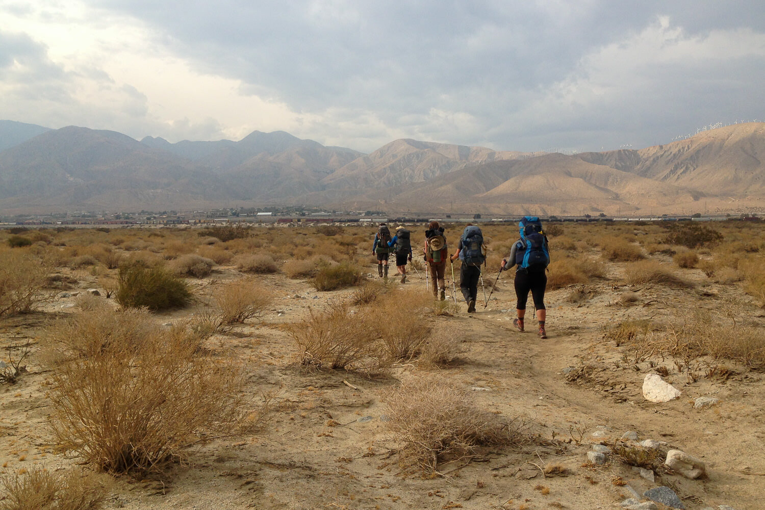 Group of thru-hikers walking through the desert toward a town.