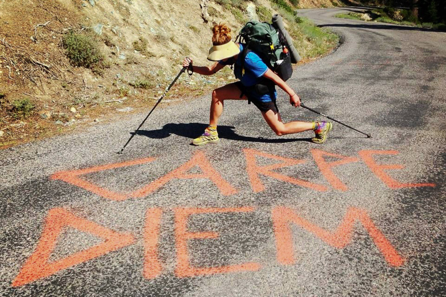 Backpacker hiking on a paved road with the note carpe diem spray painted on the road.