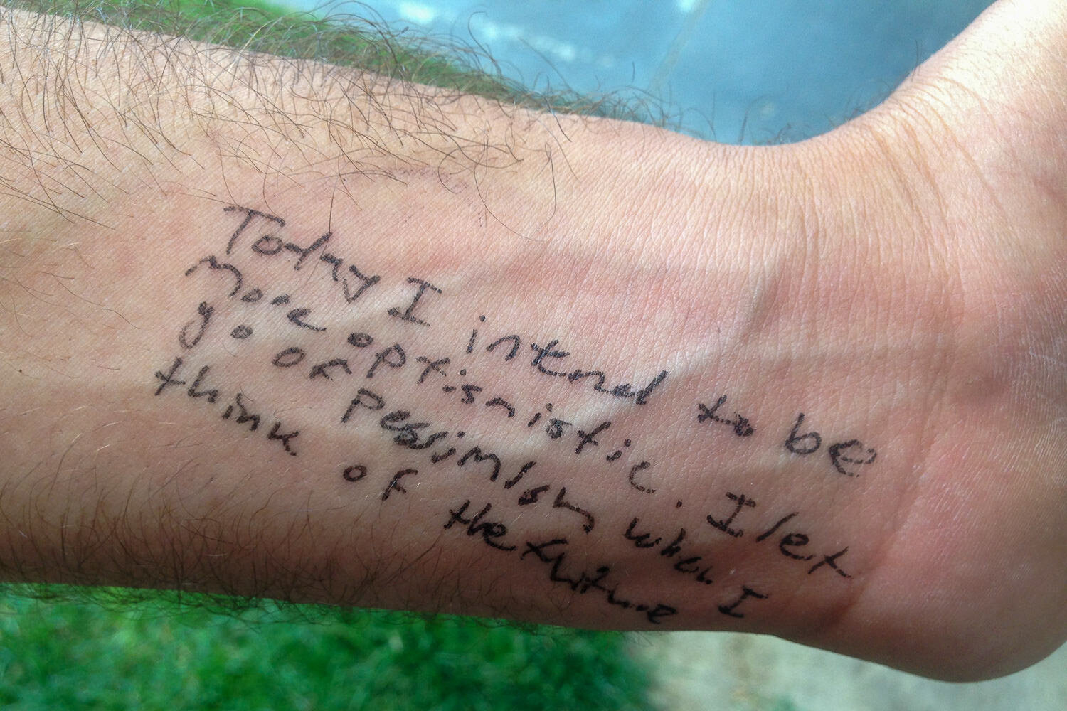 Written with ink on a wrist with the text, "Today I intend to be more optimistic. I let go of pessimism when I think of the future."