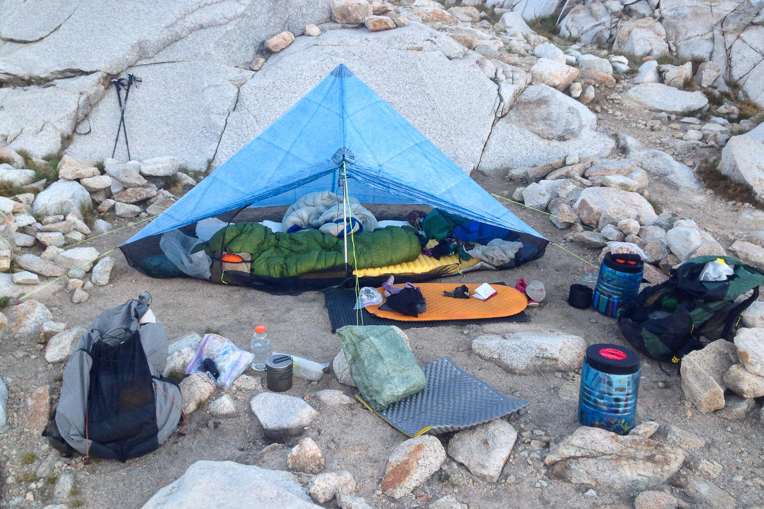 a picture of a thru-hikers campsite and gear on the ground including sleeping pad, backpack, tent, and bear canisters.