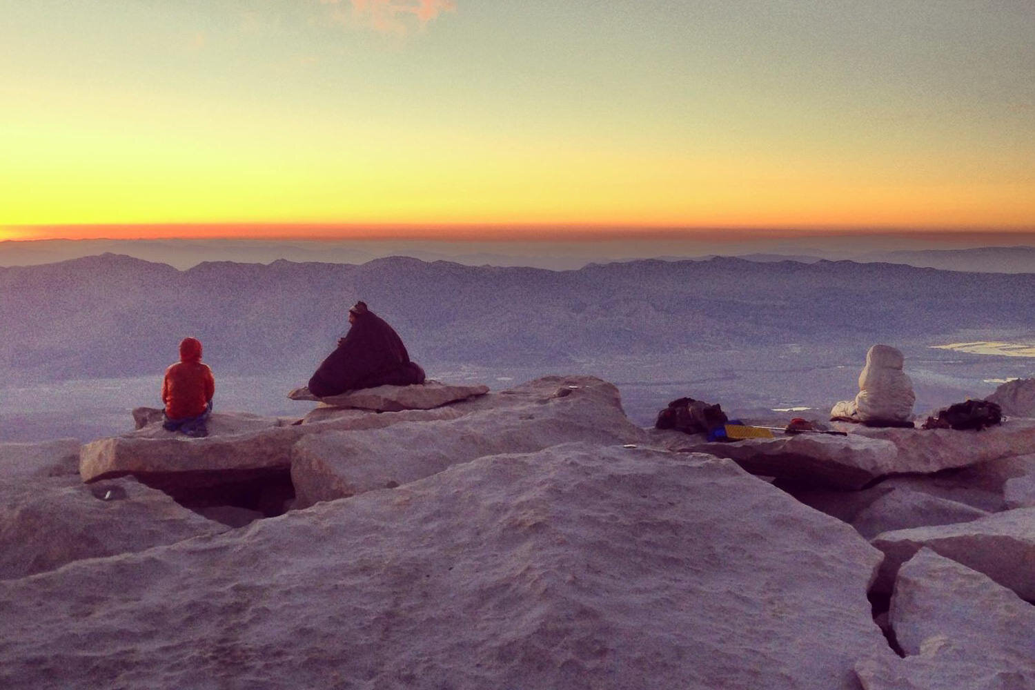 thru-hikers watch the sunrise in their sleeping bags on a rocky vista