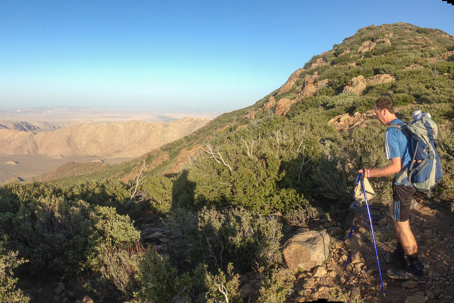 thru-hiker on the PCT on a vista overlooking a mountainous valley on a sunny day.