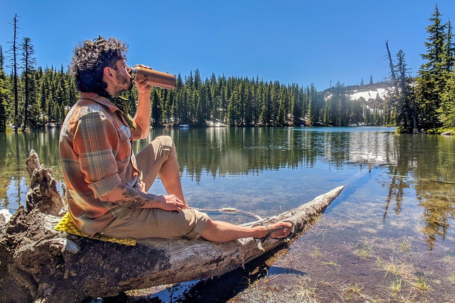 backpacker sitting on a log above a lake drinking water on the three sisters backpacking loop