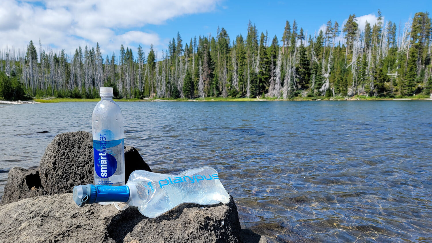 A lake with a backpacker's water filter system refilling their bottles and bladders