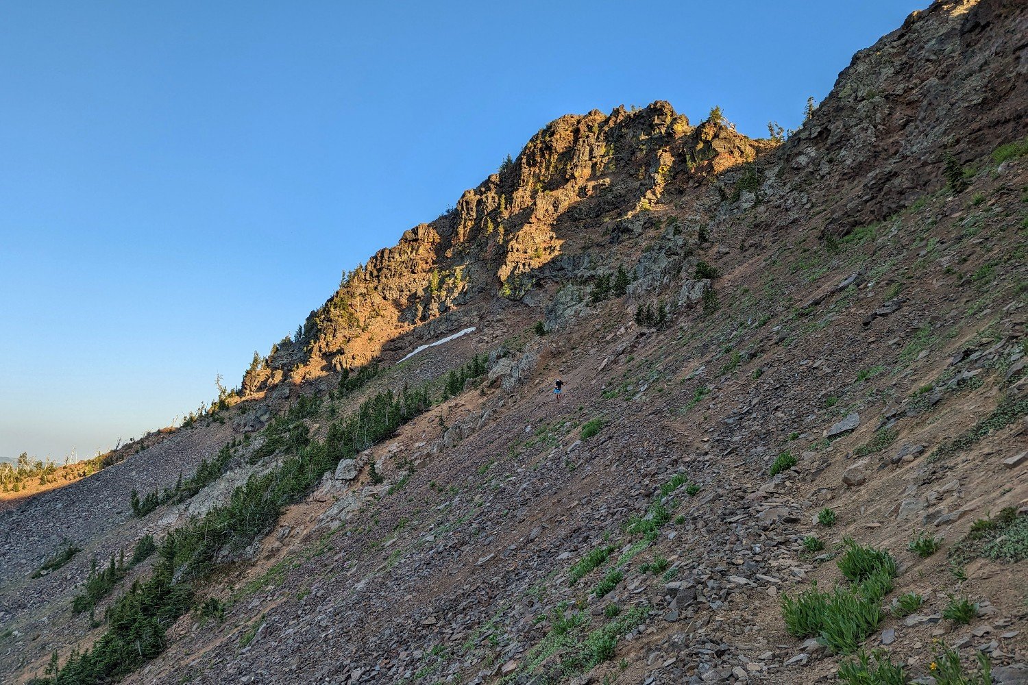 hiker traversing a steep shaded scree field in the strawberry mountains of eastern oregon