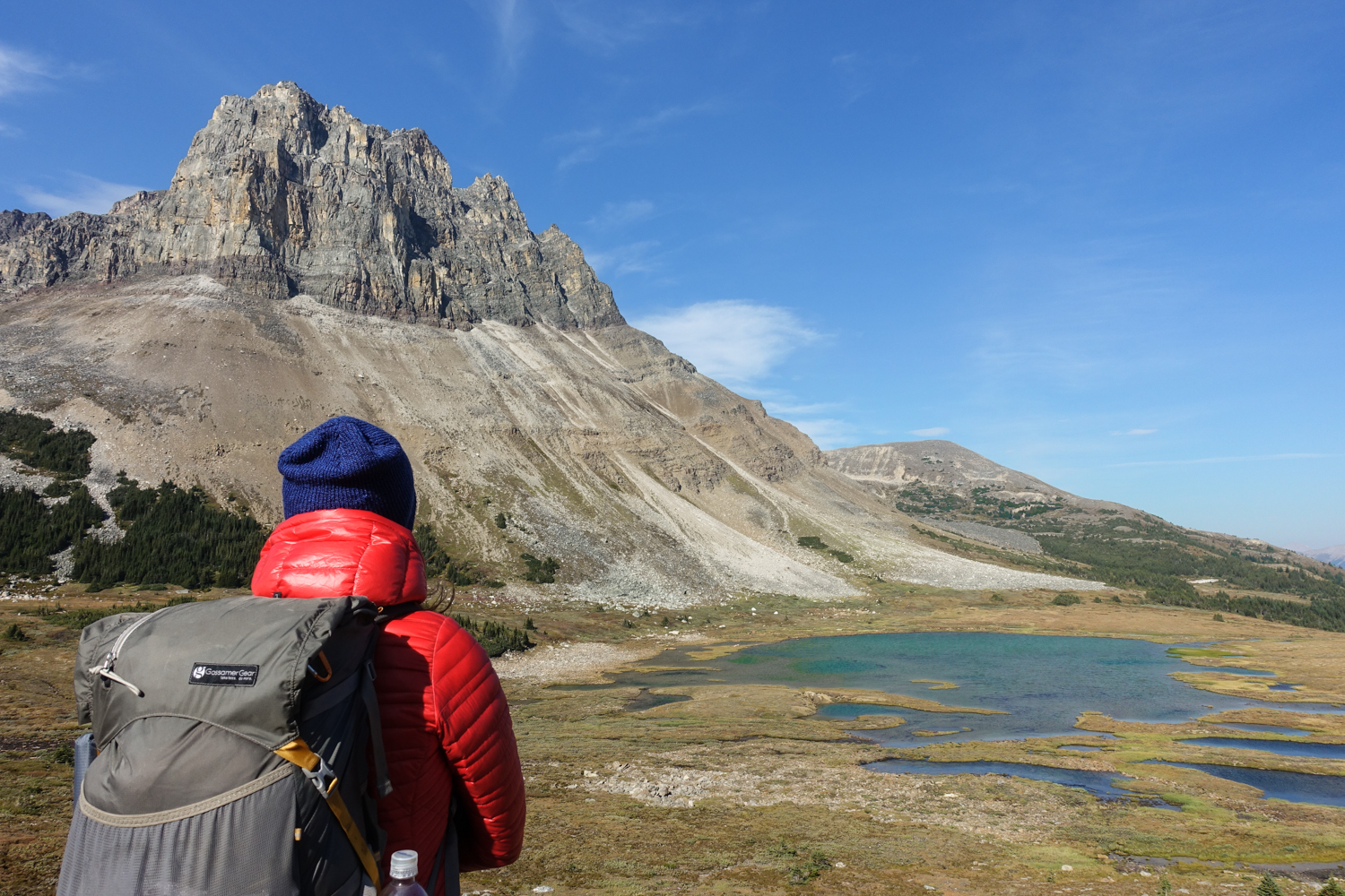 a backpacker hiking in a puffy jacket and hat as they walk toward an alpine lake beneath a spire on mount tekarra on the skyline trail in jasper national park